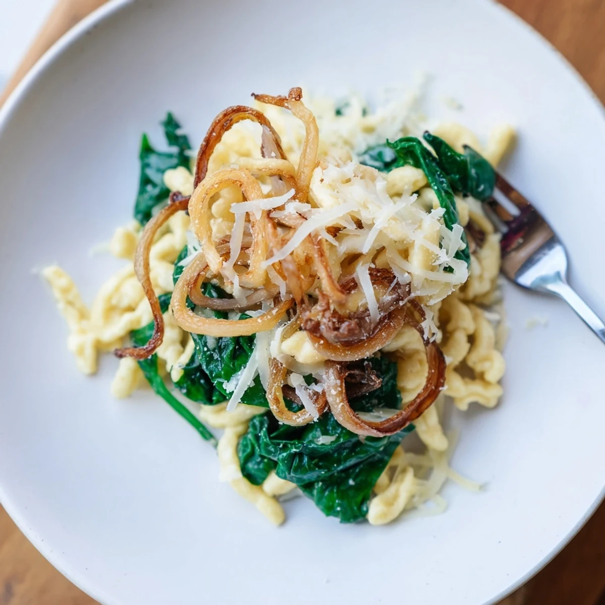 Hausgemachte Spätzle in leckerer Spinatsauce, serviert mit schmelzendem Käse und Zwiebeln.  