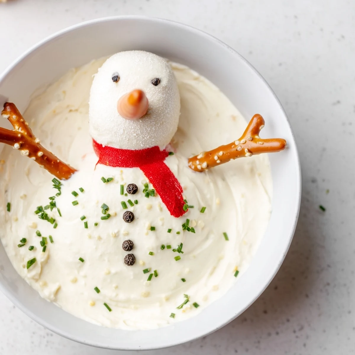 A creamy melted snowman dip bowl, ready for dipping with crackers and fresh veggies.