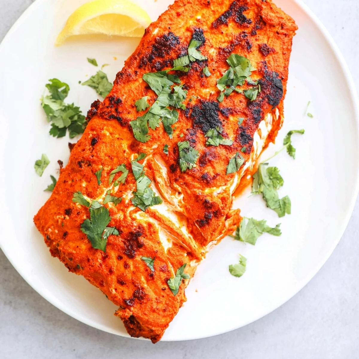 Tender Indian tikka salmon, roasted to perfection, is garnished with fresh coriander and lemon.