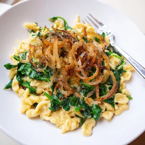 Zarte Spätzle mit Spinat und Käse, gekrönt mit knusprigen Zwiebeln für ein herzhaftes Gericht.  