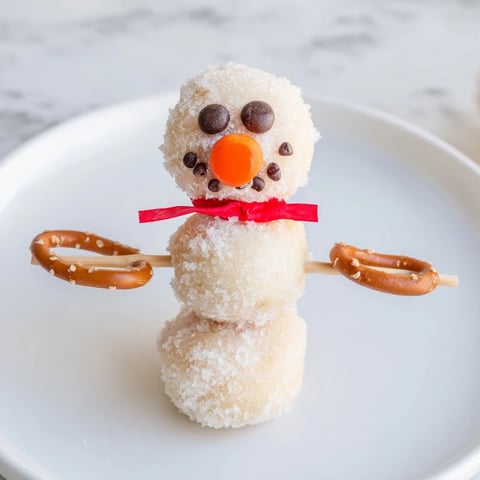 Mini Donut Snowman Stack: charming no-bake dessert featuring mini donuts stacked high with candy eyes and pretzels.