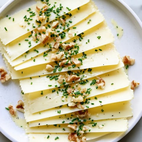 Close-up of a layered Swiss cheese slice fan, garnished with fresh chives, a flavorful snack.