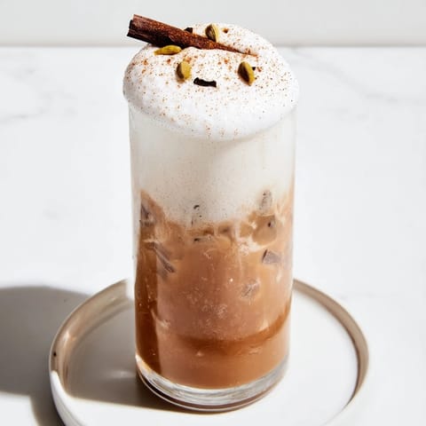 A tall glass of homemade iced chai, featuring a thick, white cold foam topping.