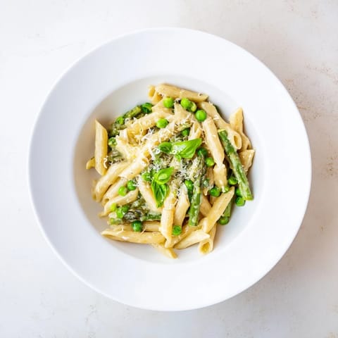 Ein farbenfroher Teller mit mit Knoblauch-Parmesan-Pasta, der von frischen Spargelspitzen, Erbsen und grünen Bohnen umrahmt wird.