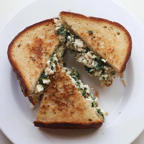 Goldbraunes, knuspriges Feta & Spinach Stuffed Grilled Cheese mit geschmolzenem Käse, ausgerollt auf einer Holzplatte.