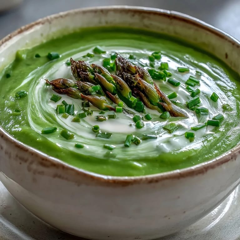 Warm Asparagus Soup with a swirl of cream, beside crusty artisanal bread slices.