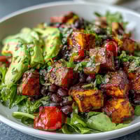 Röstaromen aus dem Ofen: gebratene Süßkartoffeln mit schwarzen Bohnen und cremigem Avocado im Schüsselbild, perfekt für ein gesundes Abendessen.